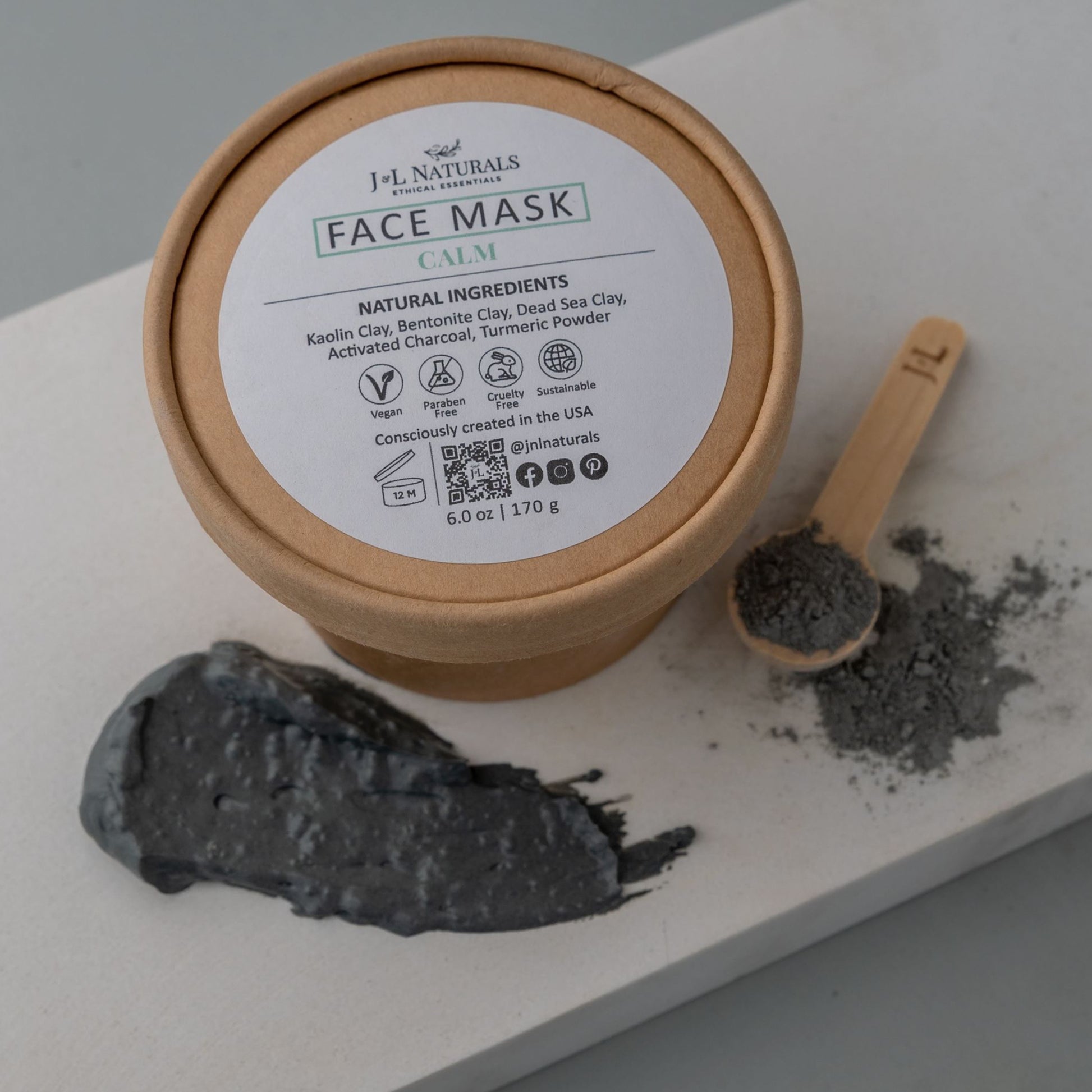 overhead shot of the container with the Calm Face Mask ingredients. A small wooden spoon is on the screen right, filled with a grey colored powder. The screen left is a dab of the powdered mask mixed with water. 
