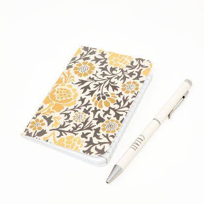 Pocket notebook 3.5x5 inches. Cover is floral pattern with yellow flowers and gray leaves. White pen sits next to the notebook.